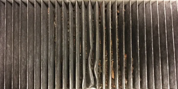 Filtro de aire dañado y sucio de la cabina con los bordes deformados y los plisados desiguales.