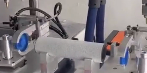 This image shows a glue application and capping machine in operation: a cylindrical workpiece is positioned on the equipment, with components around it, ready for processing.