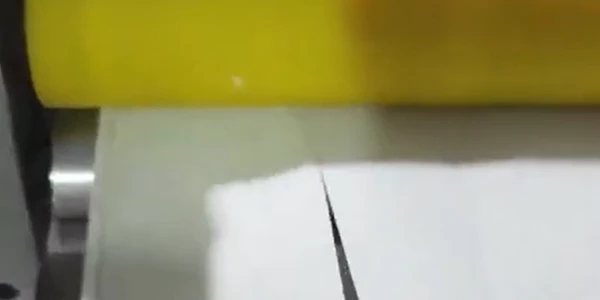 This is a cutting device slicing a white sheet, with a hand operating or retrieving the cut piece.