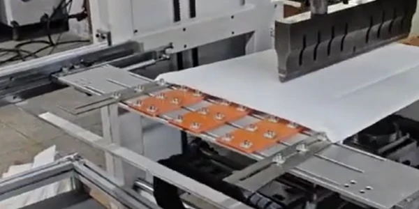 This is an online depaneling machine cutting a white sheet into panels.